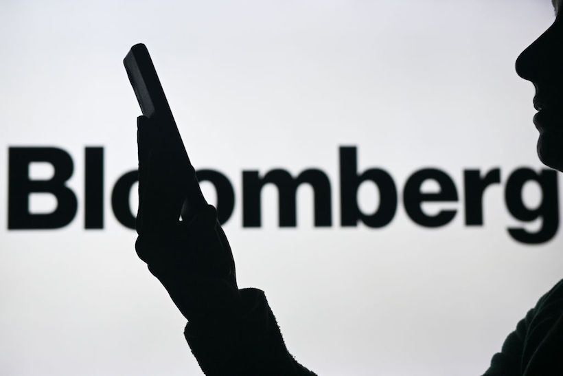 Person holding smart phone in front of Bloomberg logo