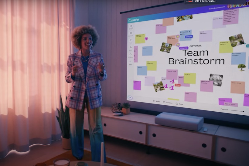 A Canva employee stands in front of a screen displaying a team brainstorming board