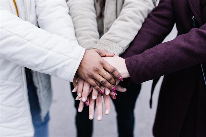 Diverse group of people placing hands together, teamwork, inclusivity concept