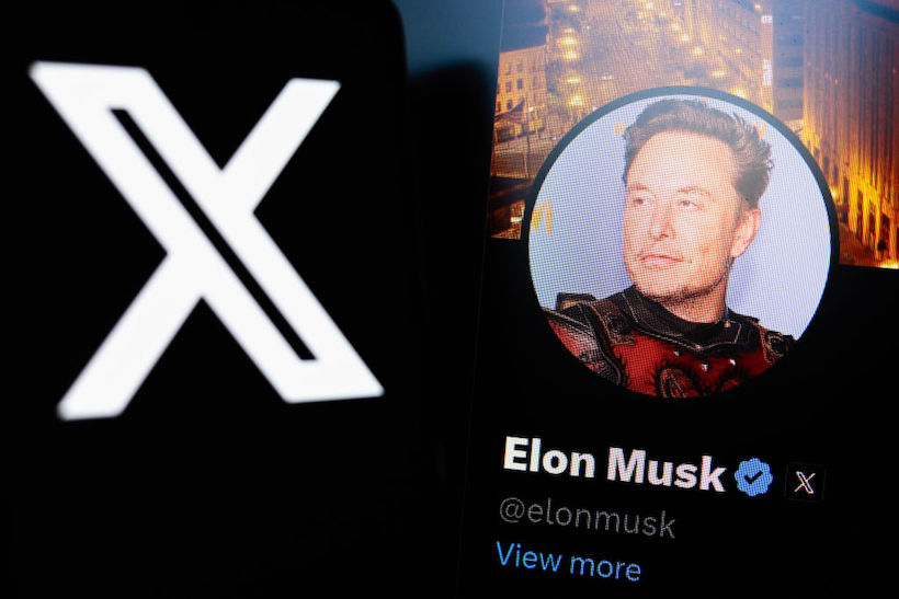 The X Twitter logo seen displayed on a smartphone with the official profile of Elon Musk, of the social network X In the background