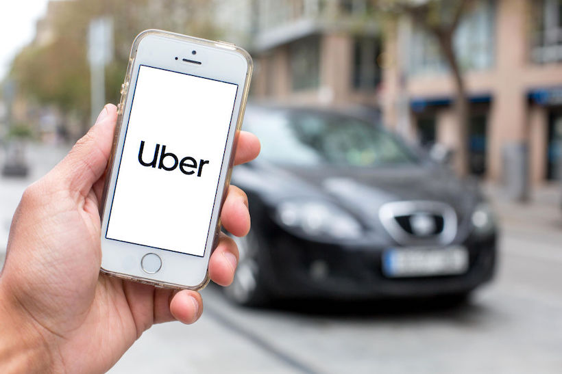 Hand holding smart phone displaying Uber logo