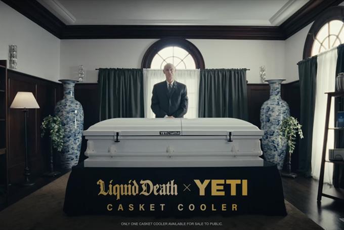 An undertaker stands behind a LiquidDeath Yeti cooler in the shape of a casket